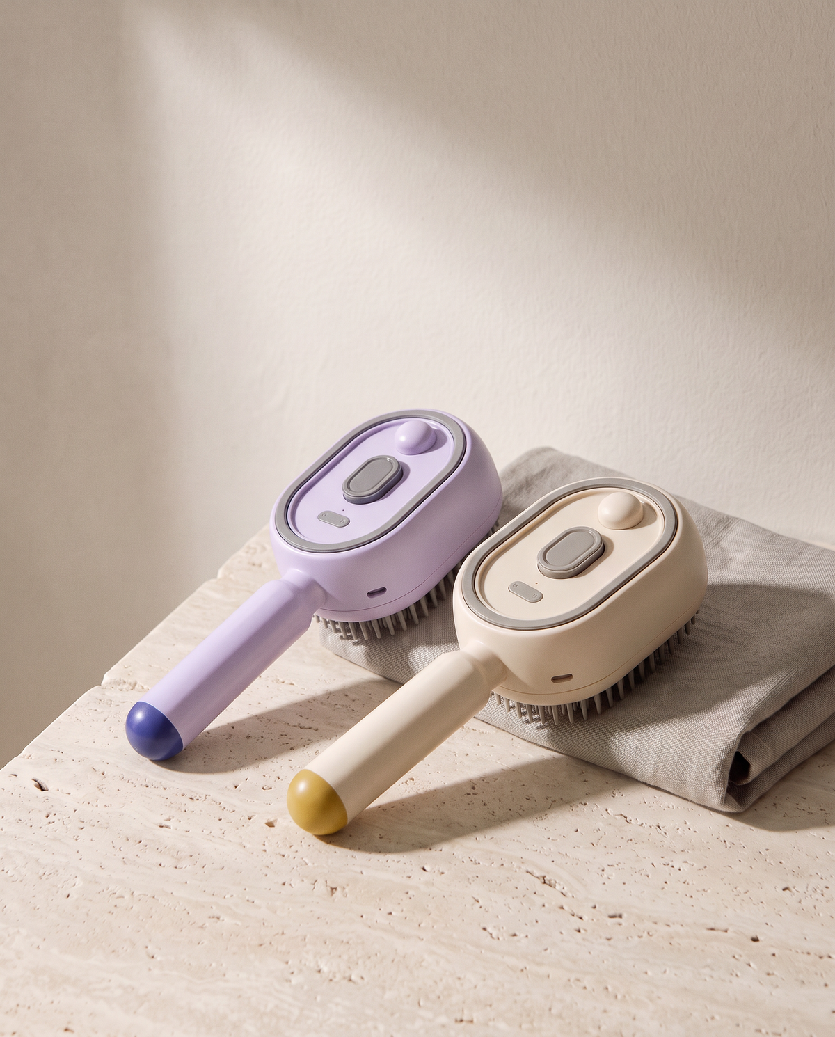 Duo de Brosses Vapo, une beige et une violette, posées sur du travertin