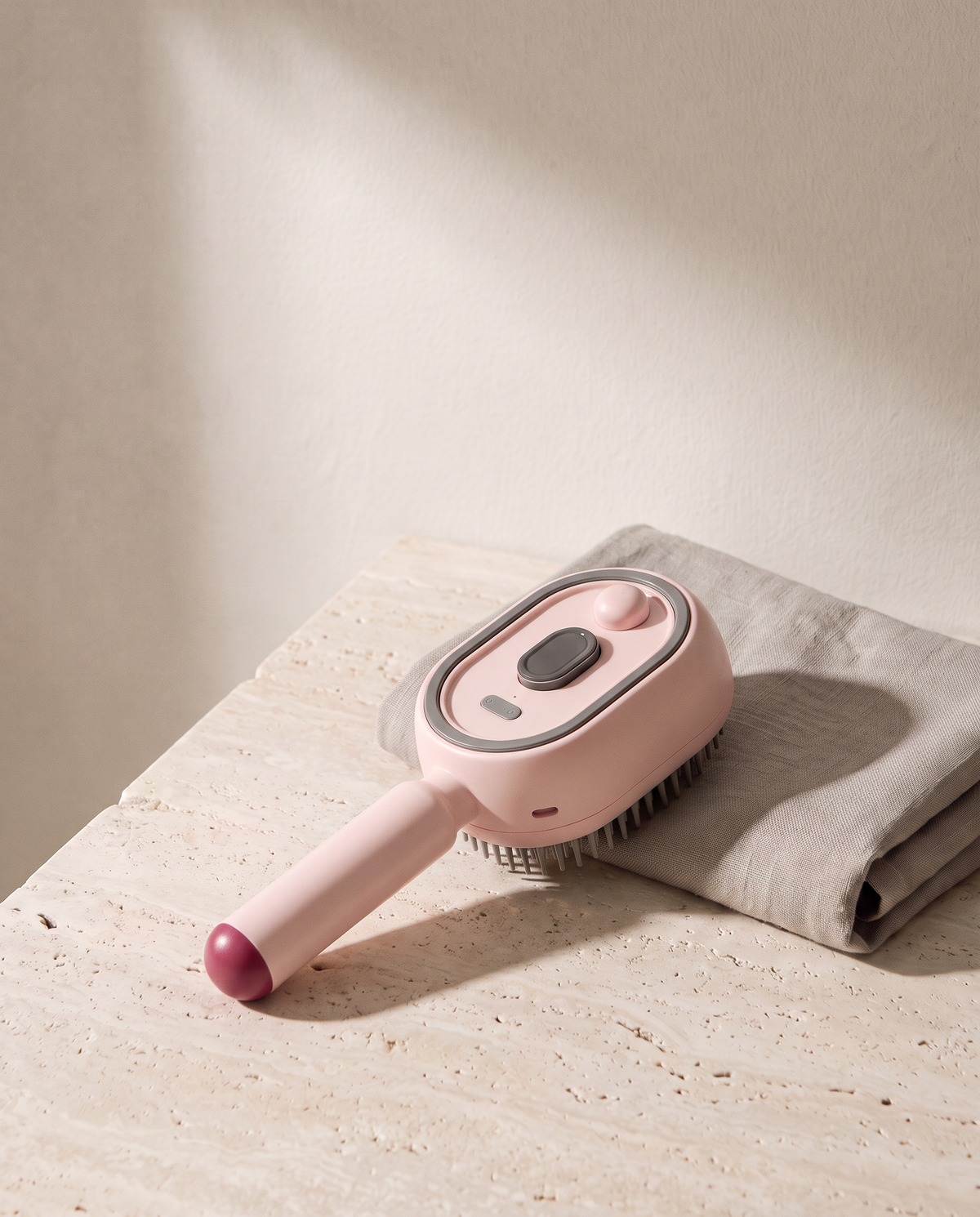 Brosse Vapo coloris rose, posée sur du travertin à côté d'une serviette en lin