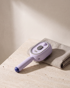 Brosse Vapo coloris violet, posée sur du travertin à côté d'une serviette en lin
