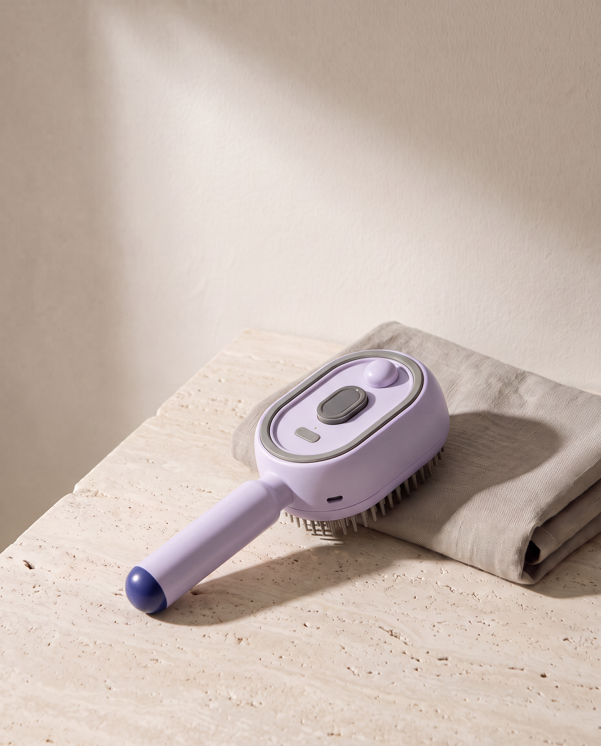 Brosse Vapo coloris violet, posée sur du travertin à côté d'une serviette en lin