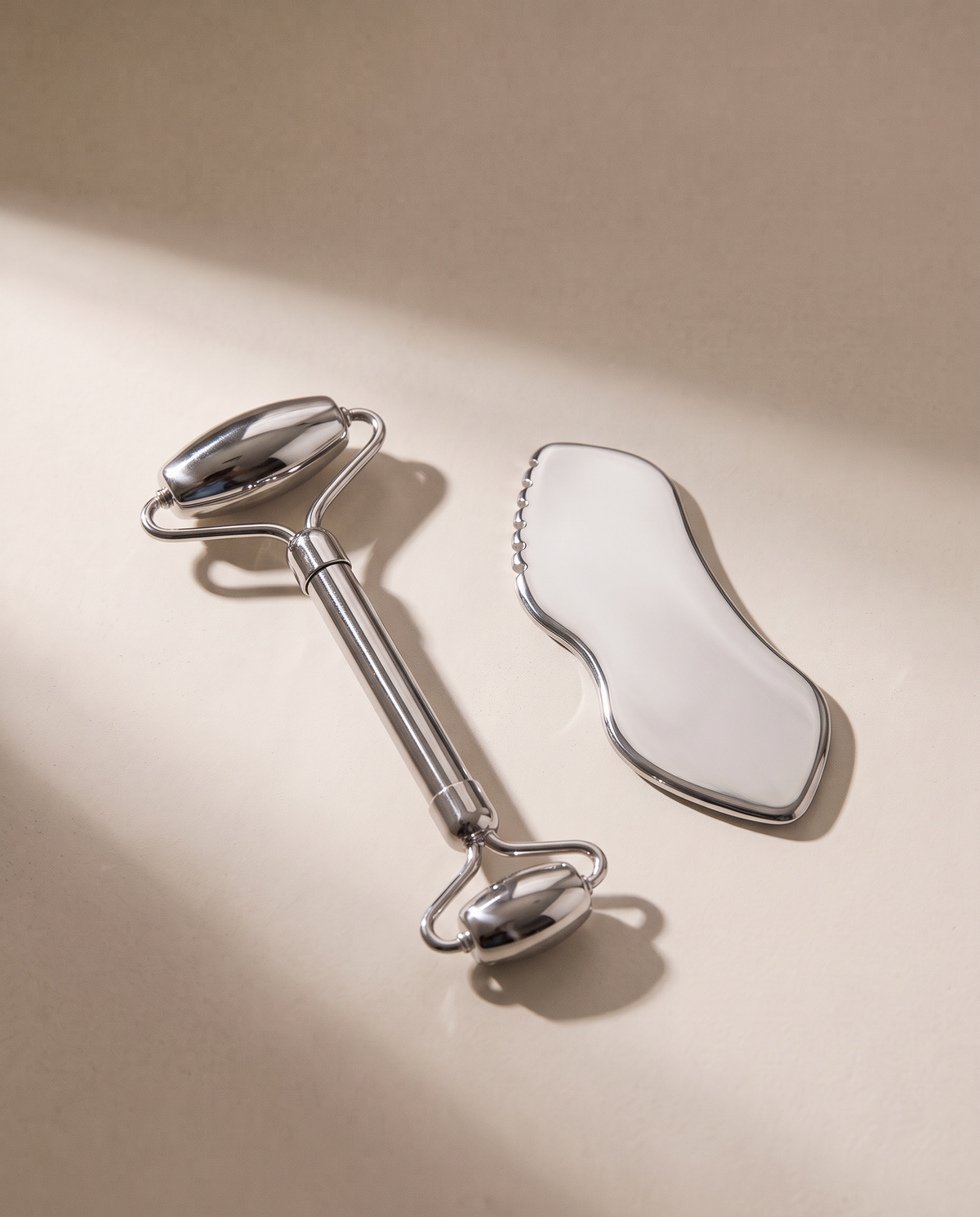 Duo SCULVORA : rouleau en acier inoxydable et gua sha vague, posés sur un enduit écru