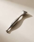 Stylo d'acupression Gua Sha Acier SCULVORA posé en diagonale sur un fond de plâtre écru