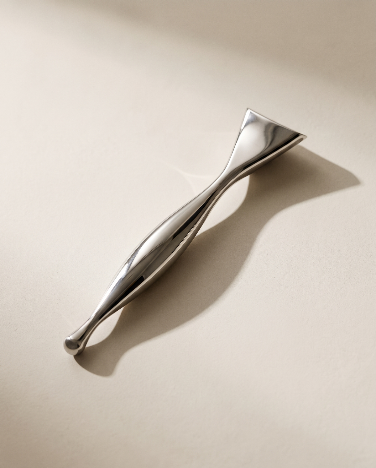 Stylo d'acupression Gua Sha Acier SCULVORA posé en diagonale sur un fond de plâtre écru