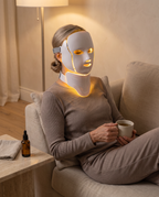 Femme avec une tisane pendant sa séance de masque LED, lumière jaune, yeux fermés