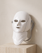 Masque LED visage et cou SCULVORA, blanc et sans fil, posé sur un bloc de travertin